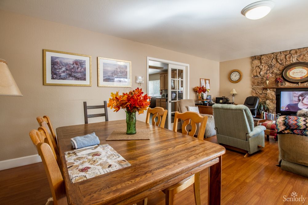 A cozy dining area with a wooden table and floral centerpiece, leading into a comfortable living space.