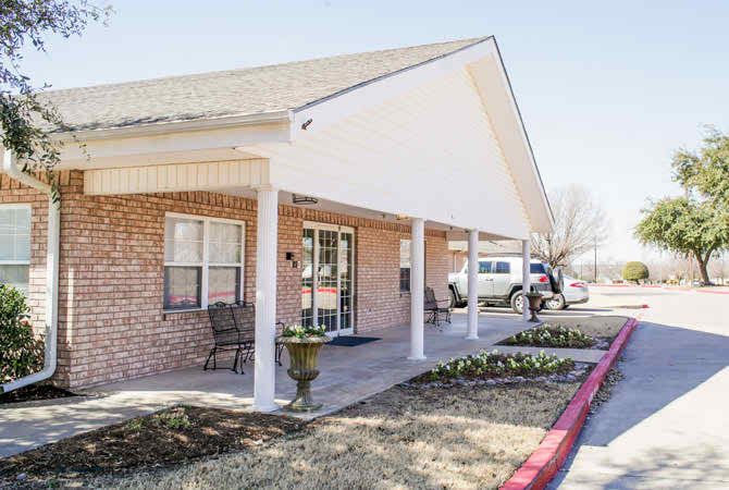 A brick building with a covered entrance and patio seating on a sunny day.