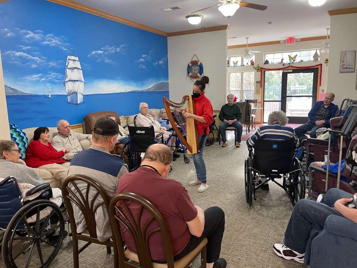 A musician playing the harp for a group of seniors in a communal setting.