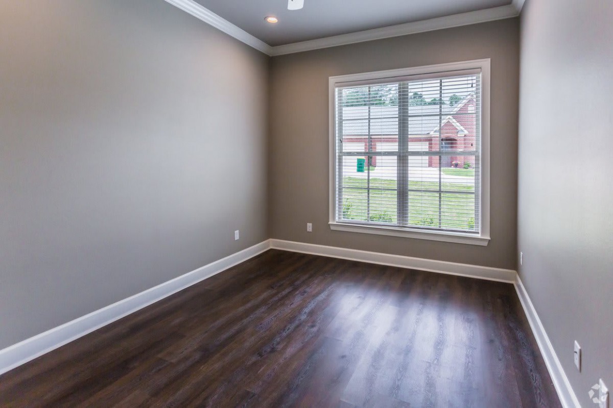An empty room with wood flooring and a large window, allowing natural light to illuminate the space.