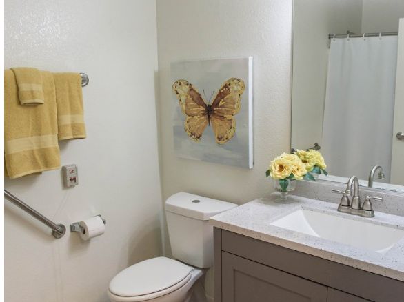 A bathroom with a butterfly painting, yellow towel, and floral decor.