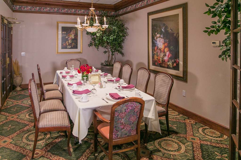 An elegantly set dining room with a table for eight, featuring a chandelier, artwork, and floral decorations.