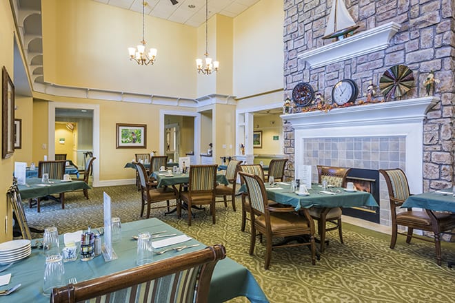 A cozy dining room with neatly arranged tables and chairs, featuring a stone fireplace and nautical decor.