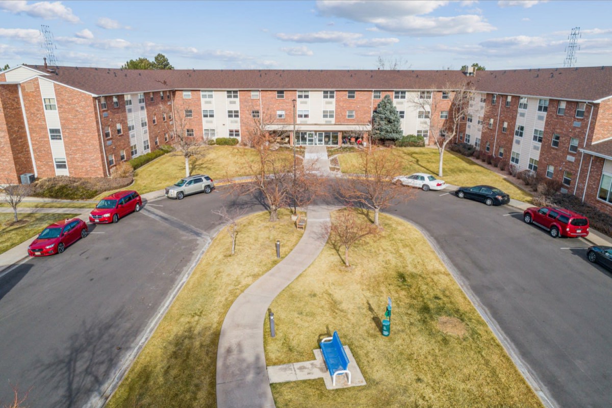 Aerial view of a brick apartment building with a circular driveway and parked cars.