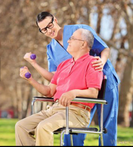 A caregiver encourages an elderly man in a wheelchair to exercise with light weights in a park setting.