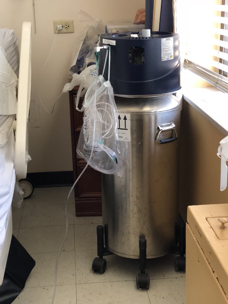 A medical oxygen cylinder with attached tubing in a hospital room.