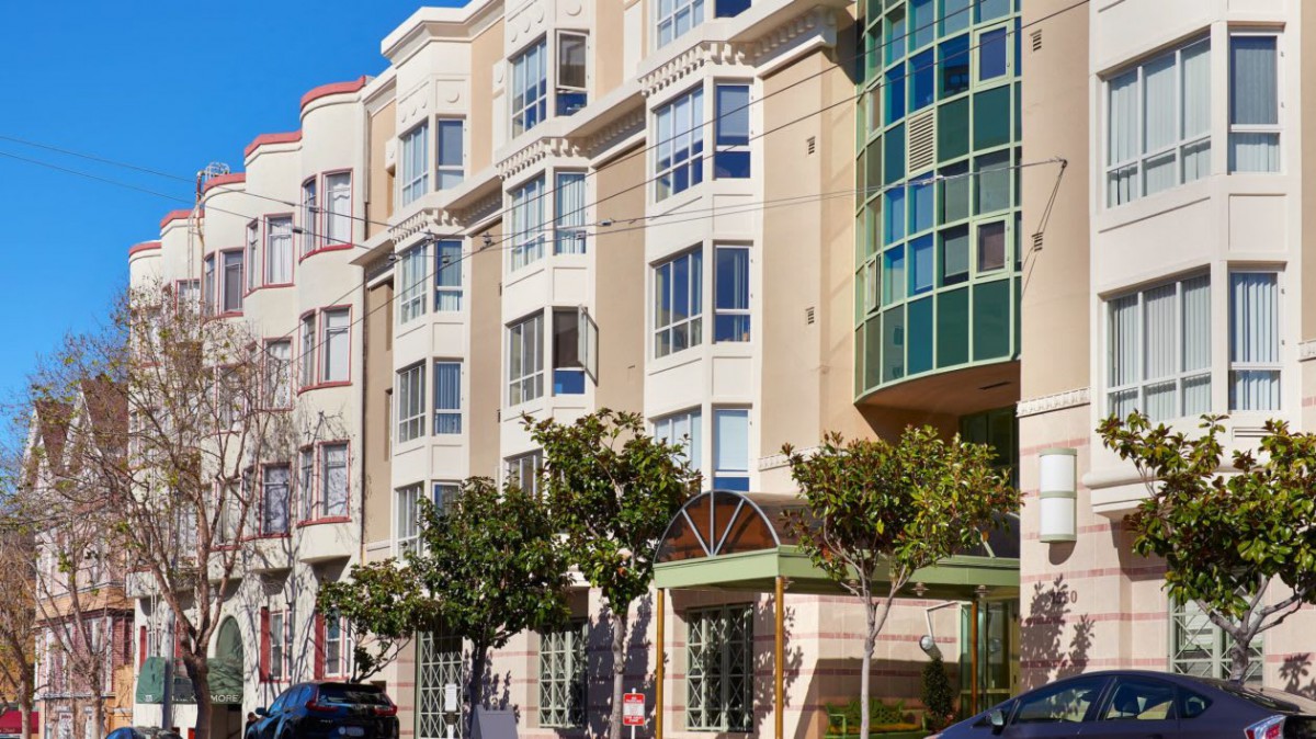 A street view of a modern residential building with large windows and trees lining the sidewalk.