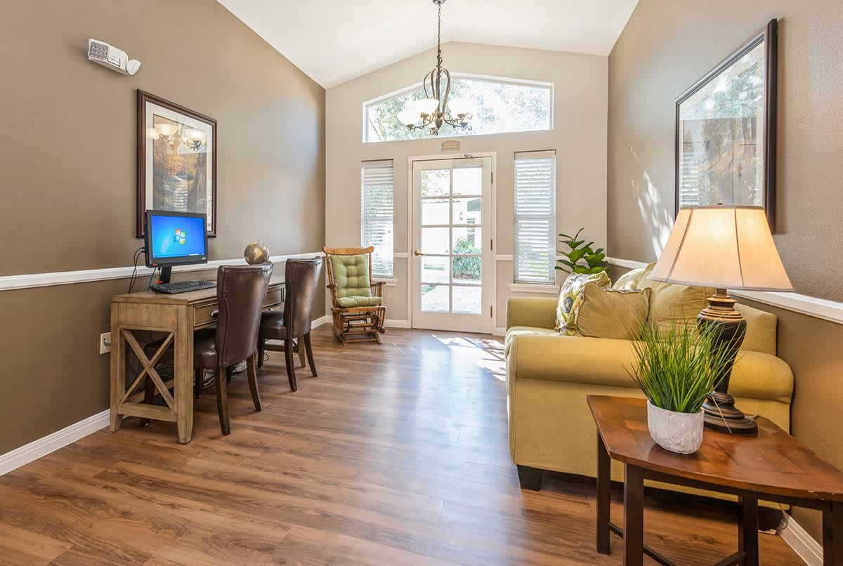 A well-lit living room with a home office setup featuring wood flooring, a computer desk, and comfortable seating.