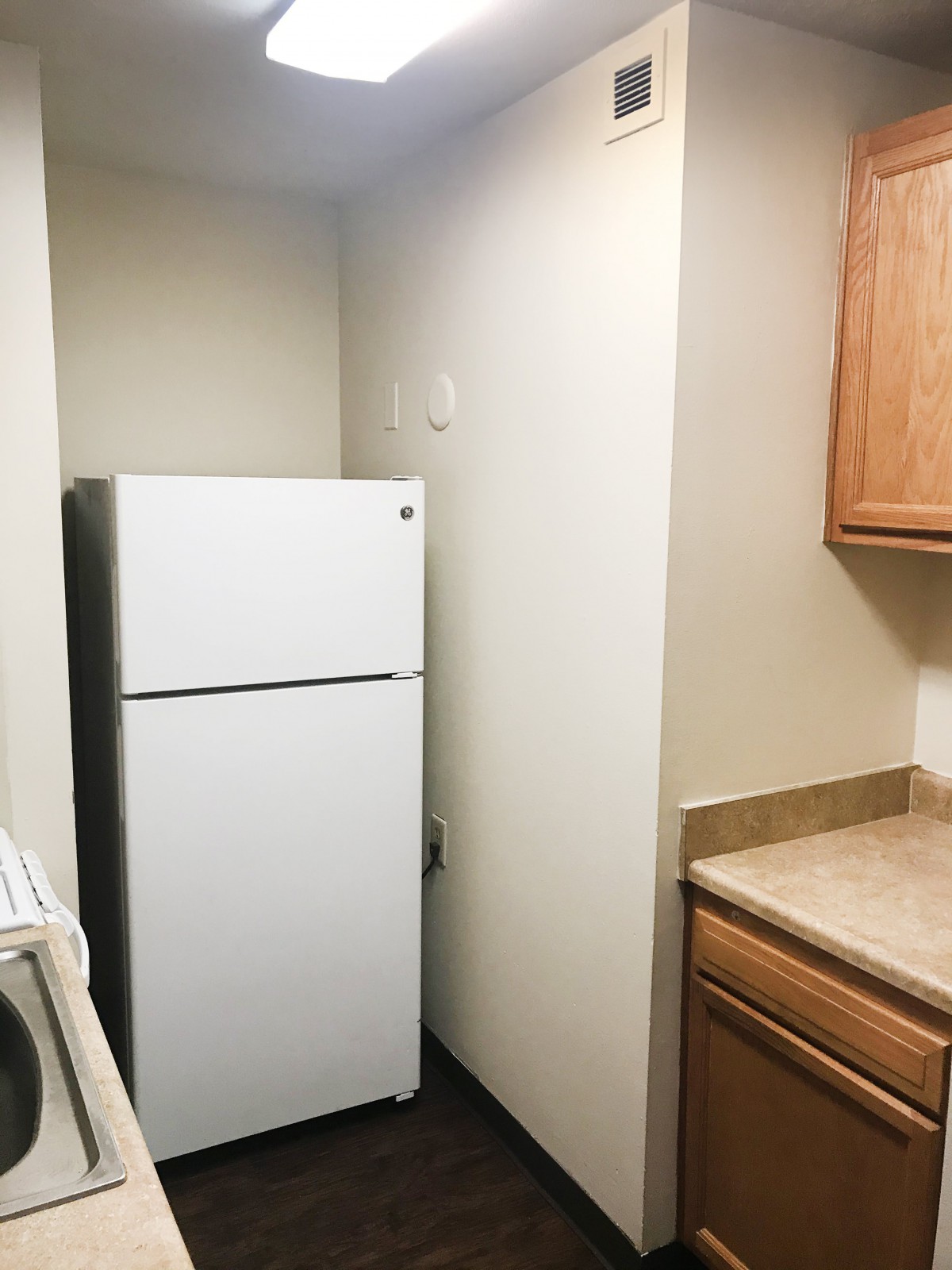 A compact kitchen space featuring a white refrigerator snugly placed between walls, with wooden cabinets and countertops.