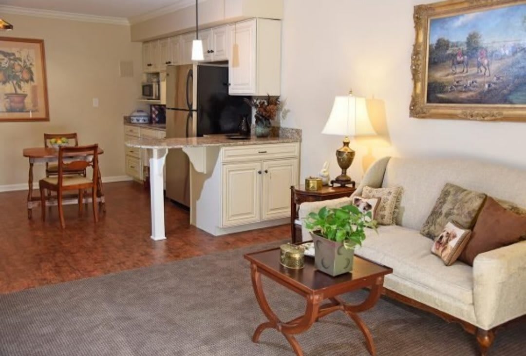 A cozy living room connected to a kitchen, featuring comfortable seating, stylish decor, and warm lighting.