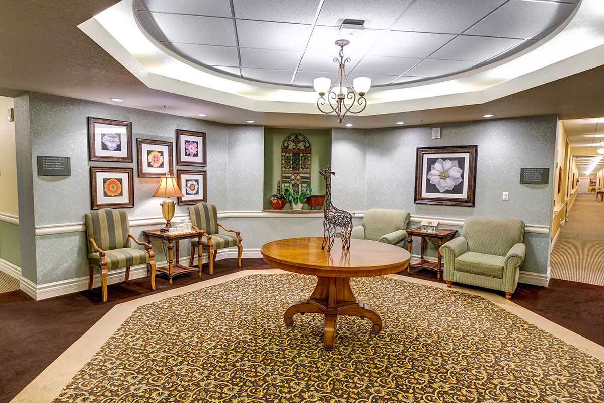 A cozy waiting room with elegant furniture, artwork on the walls, and a central chandelier.