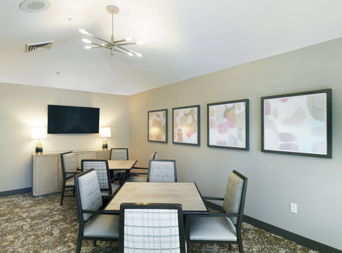 A modern meeting room with tables and chairs, decorated with artwork and equipped with a television.