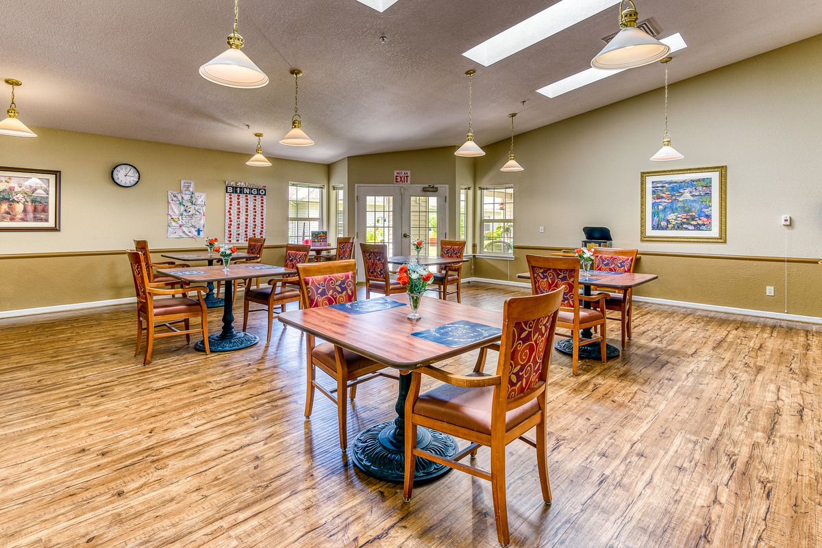 A dining area with wooden tables and chairs, well-lit by ceiling lights and natural light.