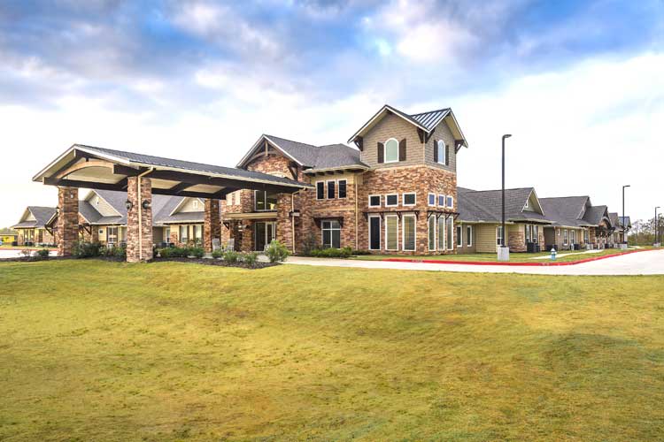 A large brick residential building with a well-maintained lawn under a partly cloudy sky.