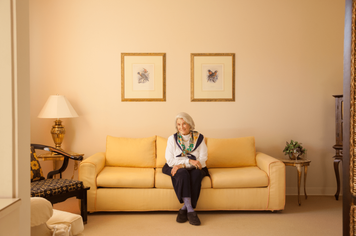 An elderly woman sitting on a sofa in a well-decorated living room.