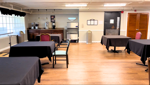 A spacious and simple dining area with neatly arranged tables and chairs, featuring a coffee station in the background.