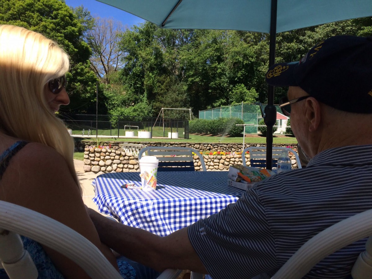 Two people sitting at a table under an umbrella in a park setting.