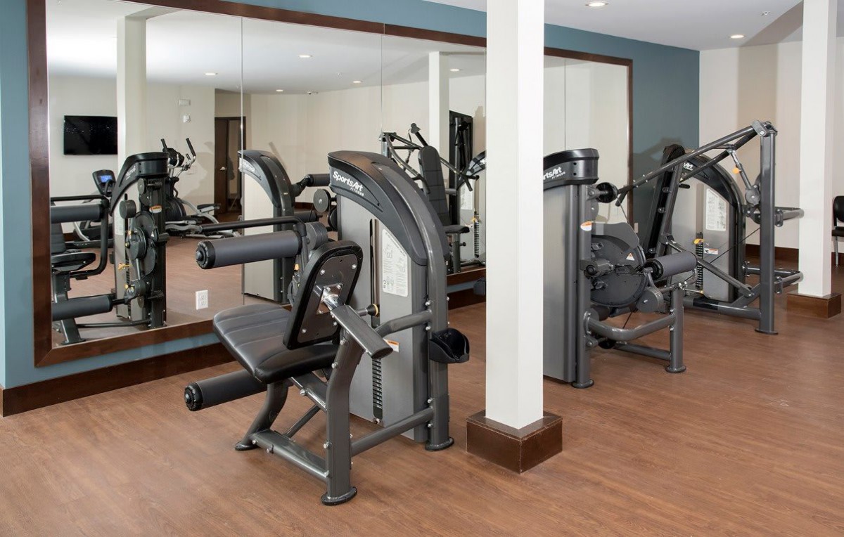 A gym room with exercise equipment including a leg press machine, surrounded by mirrors.