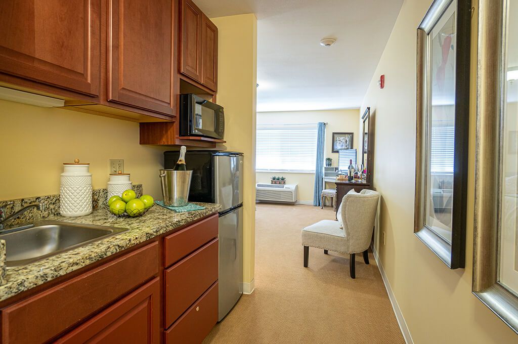 A cozy apartment interior featuring a compact kitchen area with a fridge and microwave, adjacent to a small living space with a chair.