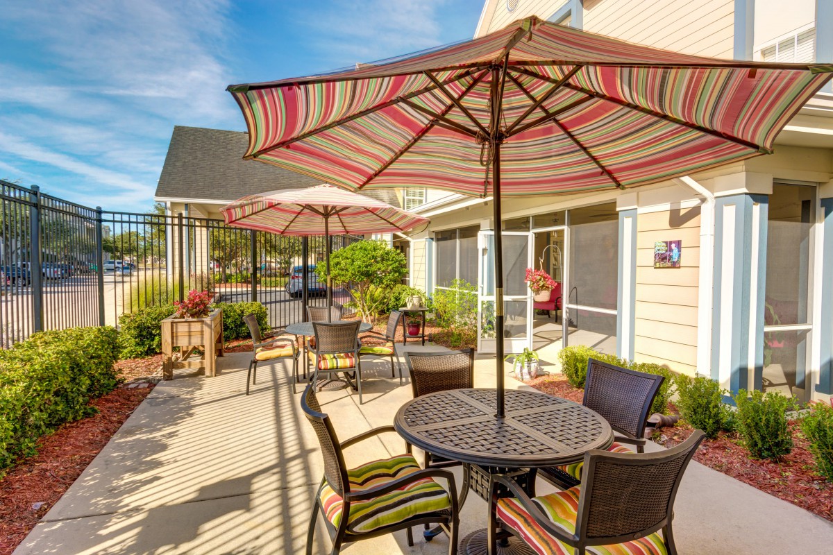A sunny outdoor patio area with tables, chairs, and striped umbrellas.