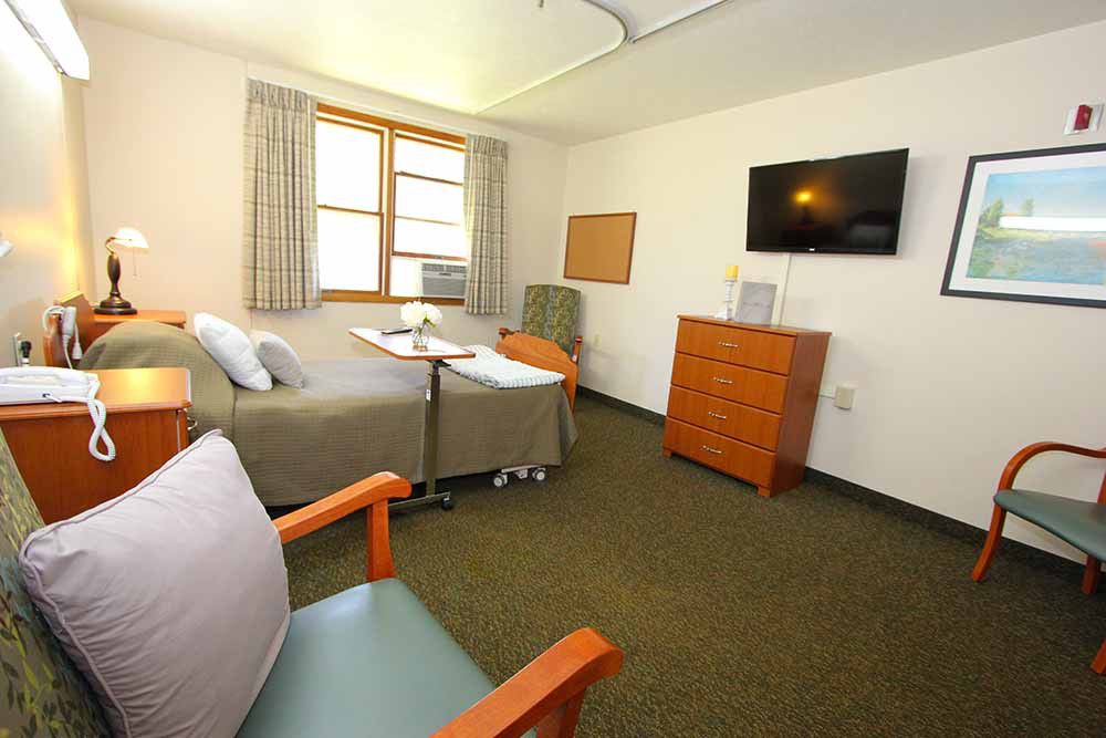 A clean and organized hospital room with a bed, chair, and mounted television.