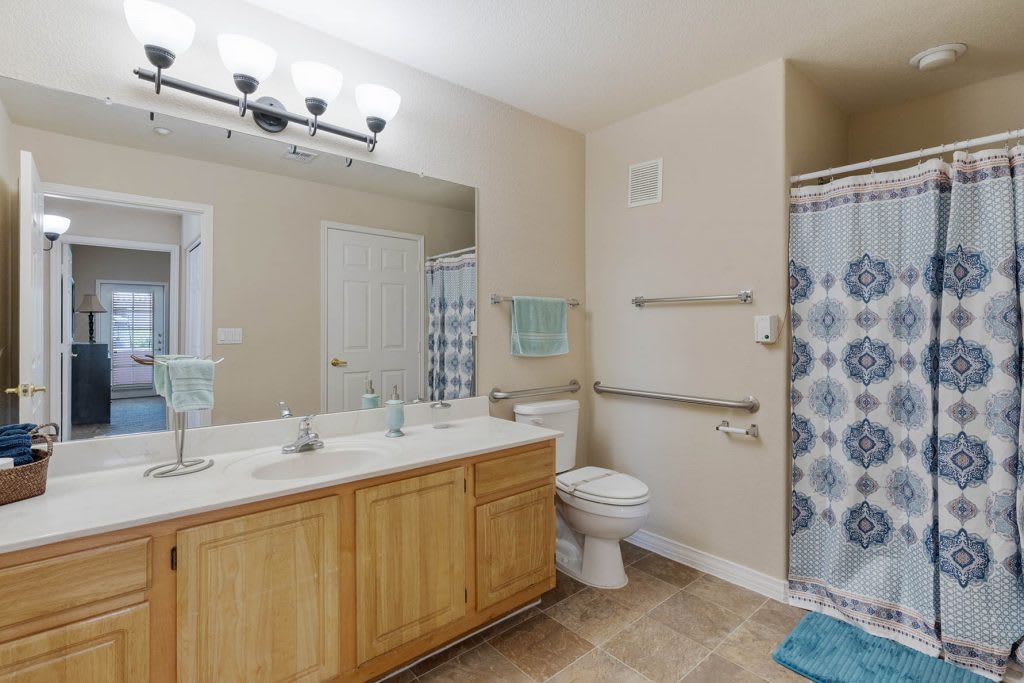 A modern bathroom featuring a large mirror, double sink, and a shower with a patterned curtain.