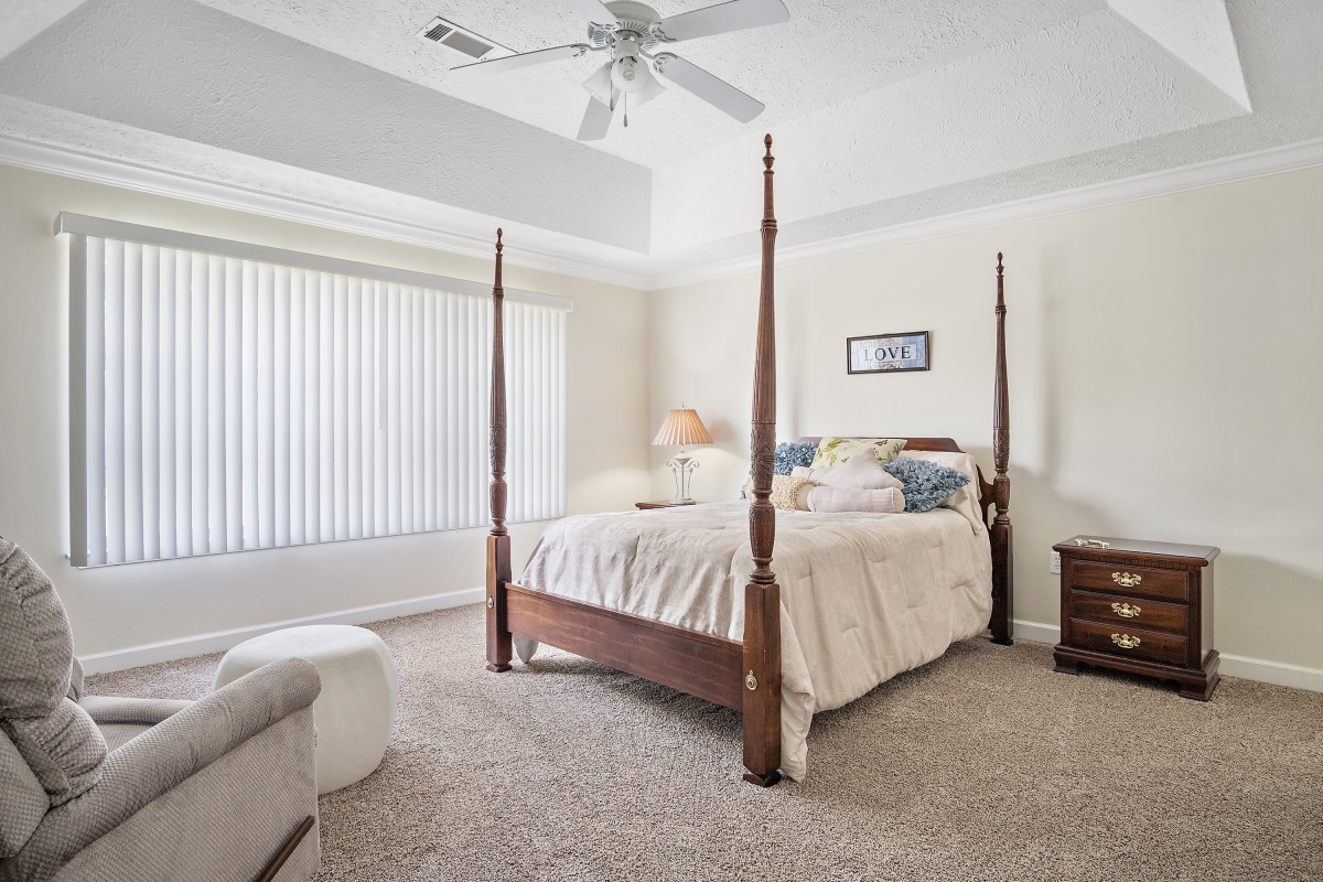 A cozy bedroom featuring a four-poster bed, soft carpeting, and a ceiling fan.