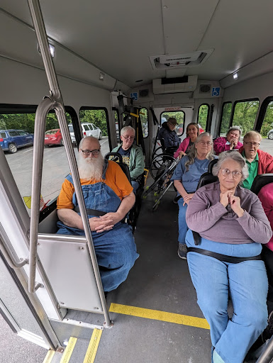A group of elderly individuals enjoying a ride on a bus, surrounded by greenery.