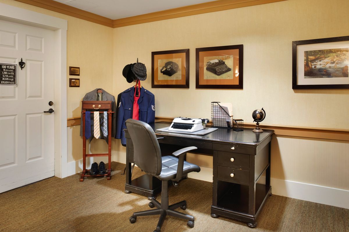 A tidy office space with a desk, chair, and typewriter, flanked by a coat stand holding ties and a suit jacket.