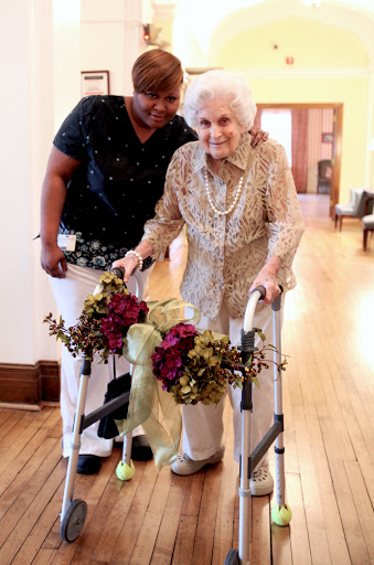 An elderly woman receiving support while using a walker, highlighting the importance of care and companionship.