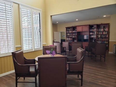 A cozy library seating area with chairs, a table, and bookshelves in the background.