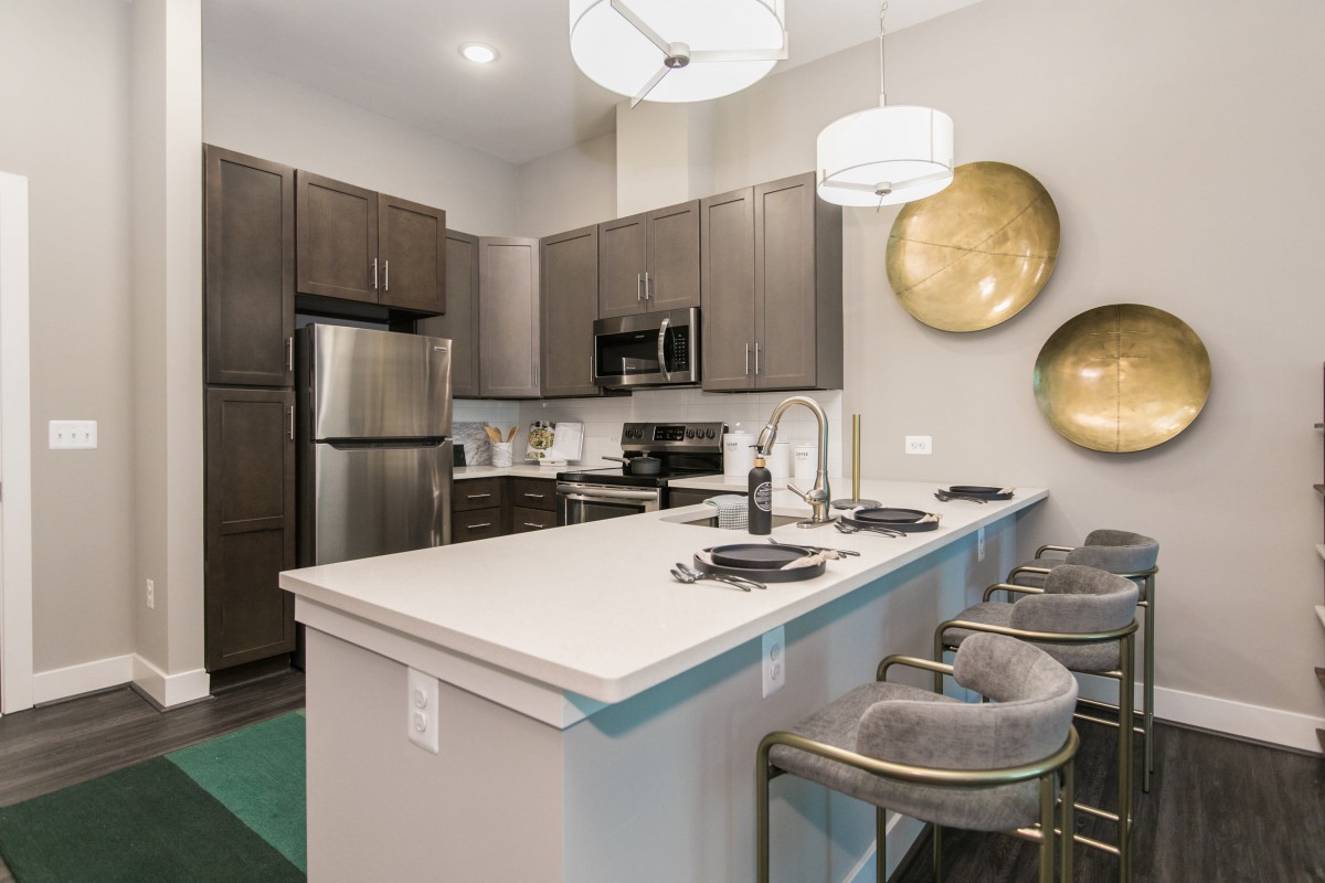 A contemporary kitchen with stainless steel appliances and a central island featuring bar stools and pendant lighting.