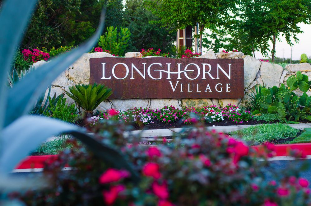 A welcoming sign for Longhorn Village surrounded by a vibrant garden.