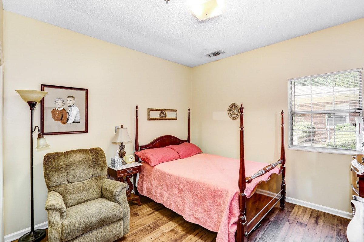 A cozy bedroom with a four-poster bed, an armchair, and wall art.