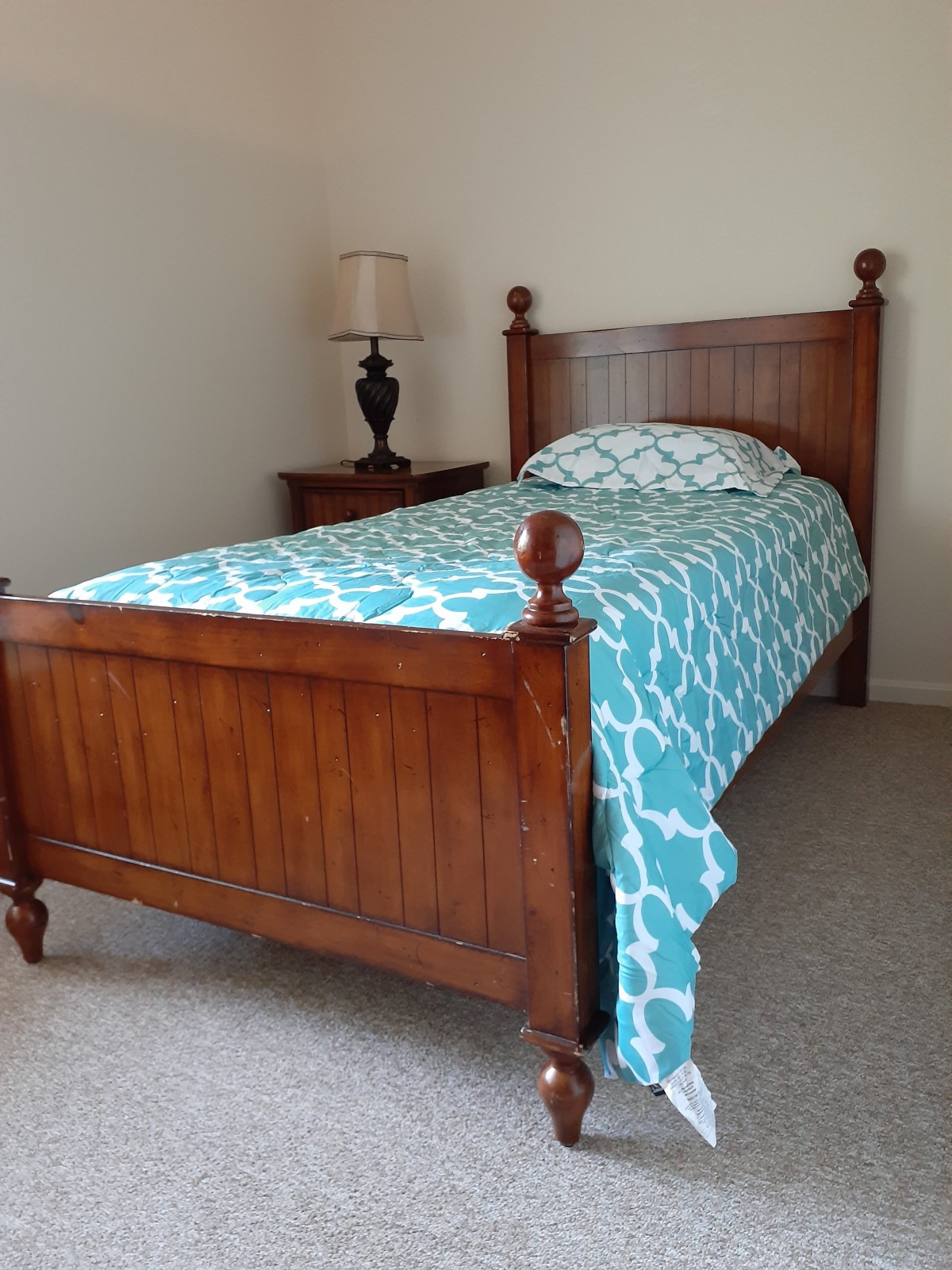 A cozy bedroom with a wooden single bed and patterned quilt.
