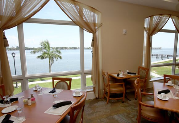 A tranquil restaurant dining area with a picturesque view of the lake through large windows, featuring tables and chairs arranged for patrons.