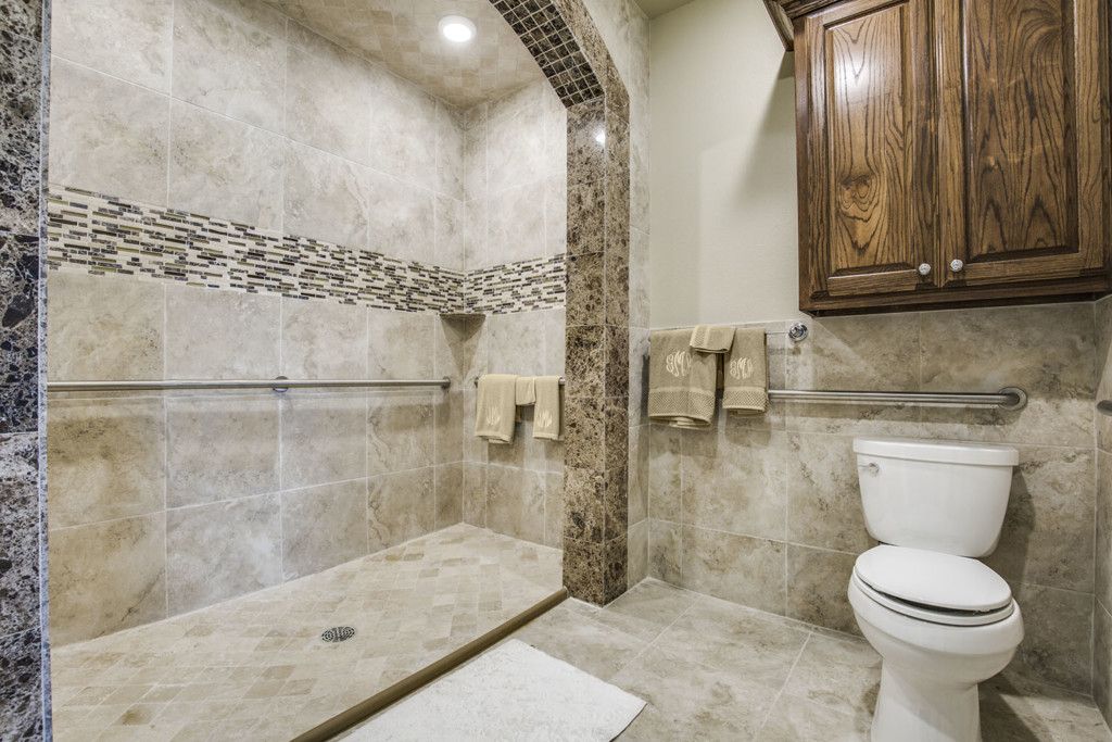 A modern bathroom featuring a tiled shower area, toilet, and wooden cabinet.