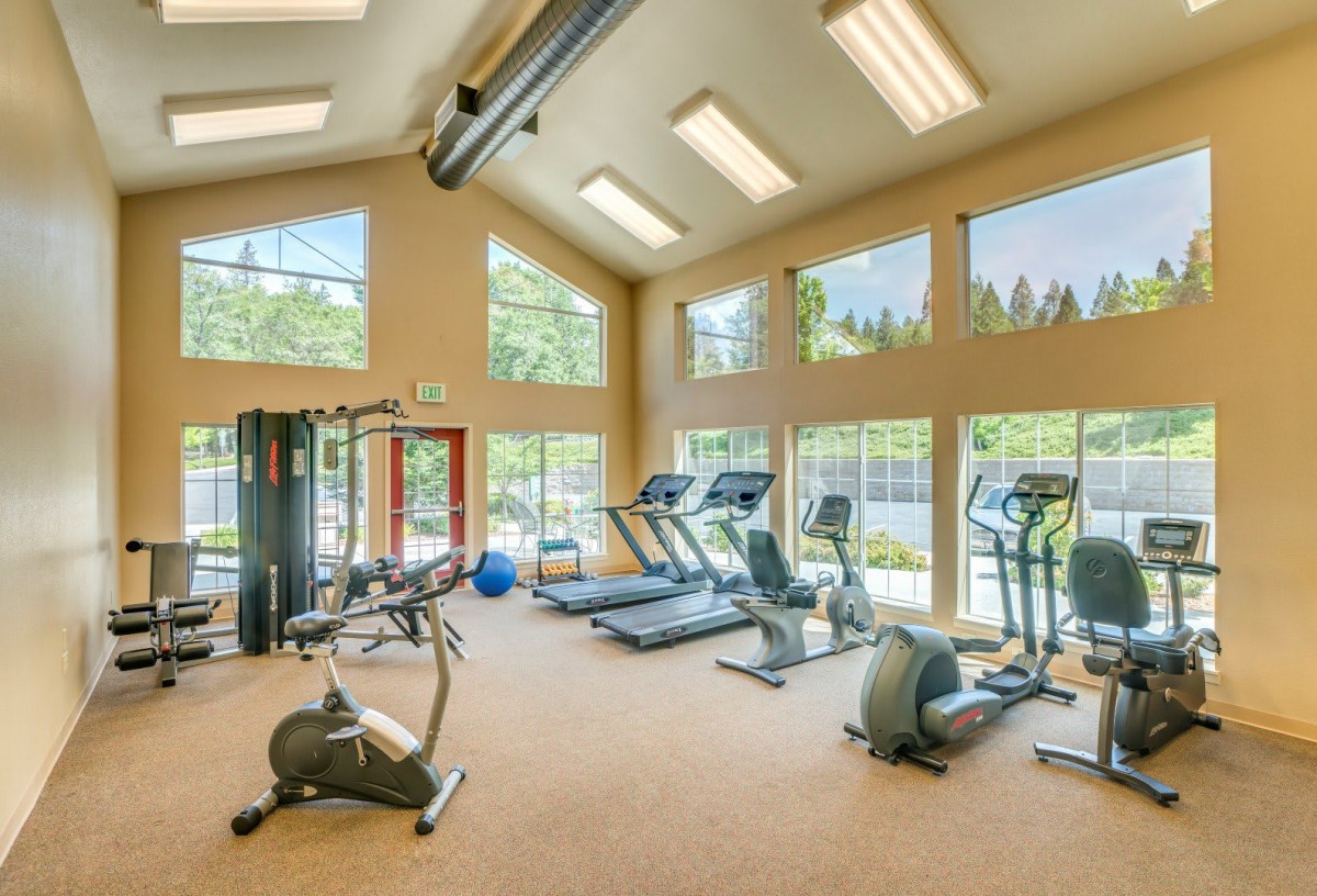 A well-lit gym with a variety of exercise equipment and large windows.