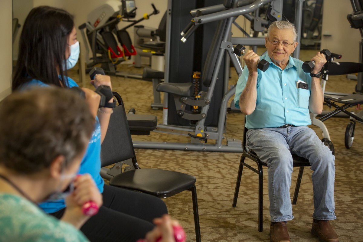 A group of seniors engaging in a seated exercise session with dumbbells in a gym setting.