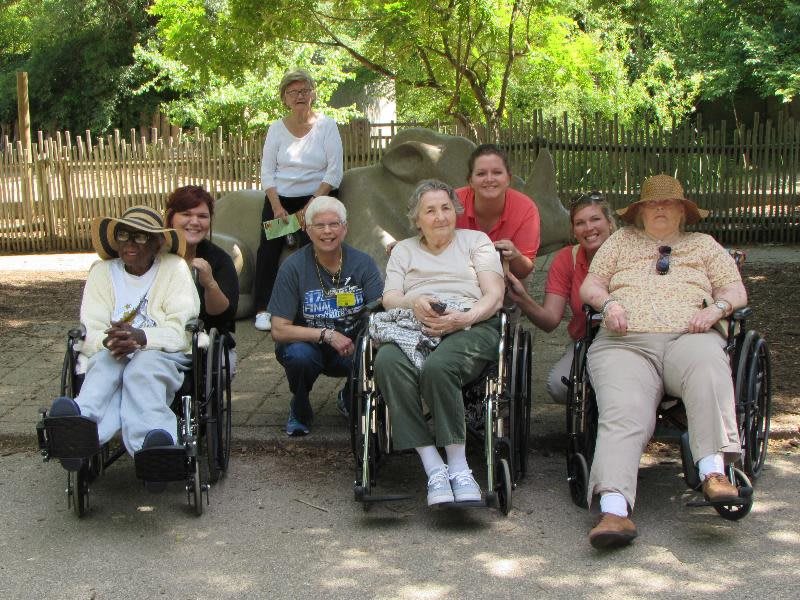 A group of people enjoying a sunny day outdoors, some seated in wheelchairs.