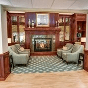 A cozy sitting area featuring a fireplace, comfortable chairs, and elegant wood paneling.