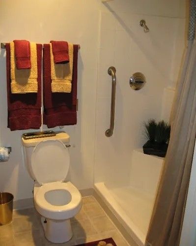 A clean bathroom featuring a toilet, shower with grab bar, and neatly arranged towels.