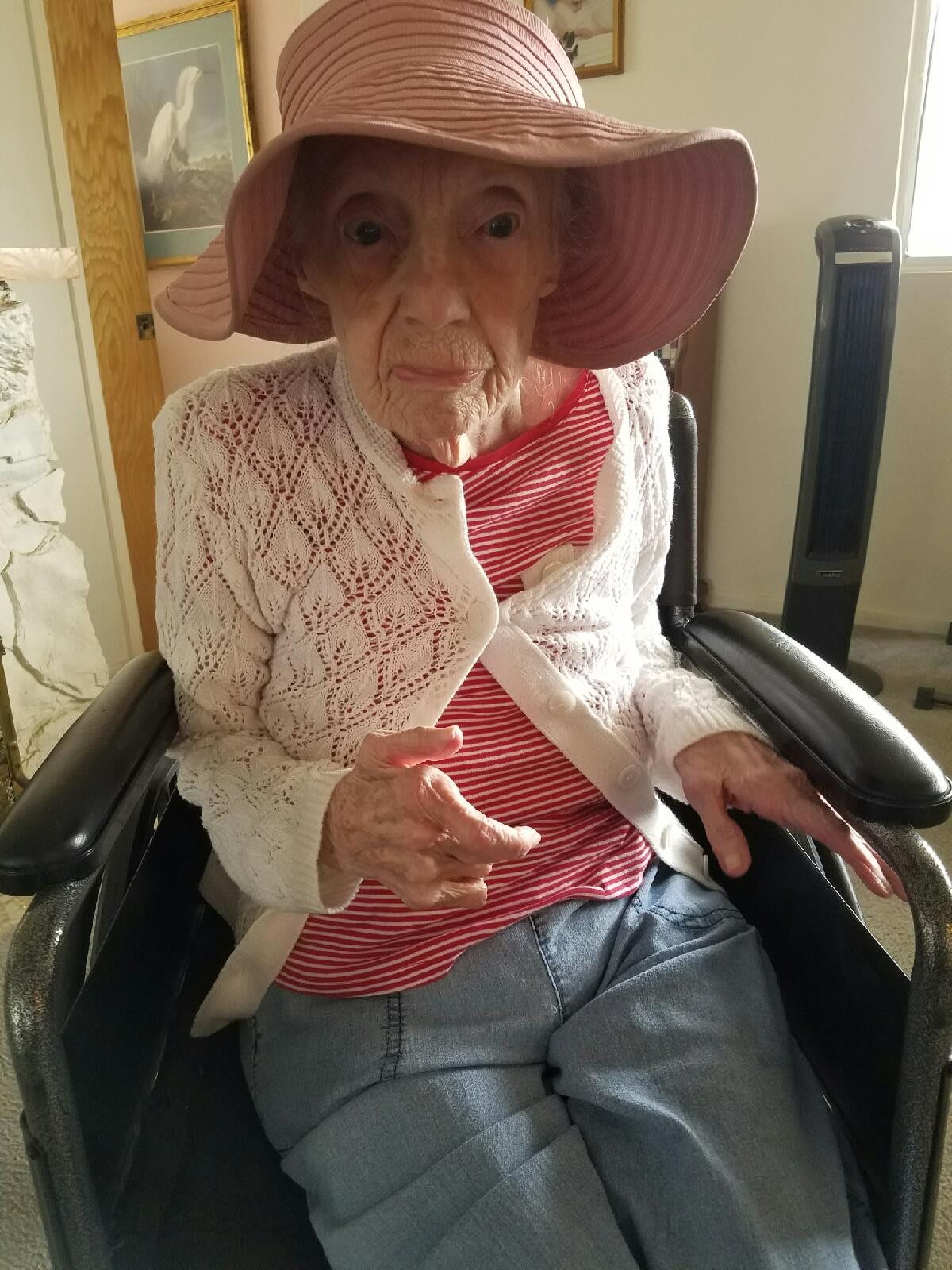 An elderly woman wearing a hat and sitting in a wheelchair indoors.