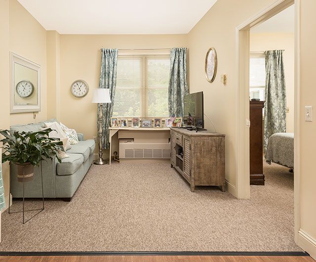 A cozy living room with a pastel sofa, wooden TV stand, and natural light coming through the windows.