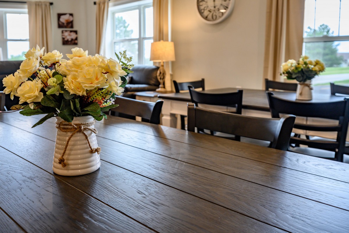 A cozy dining room with a wooden table, chairs, and a vase of yellow flowers.