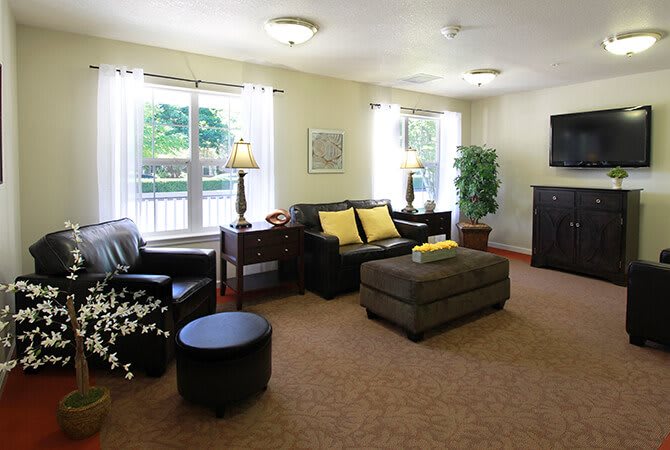 A cozy living room with a sofa, coffee table, and lamps, featuring large windows and warm decor.