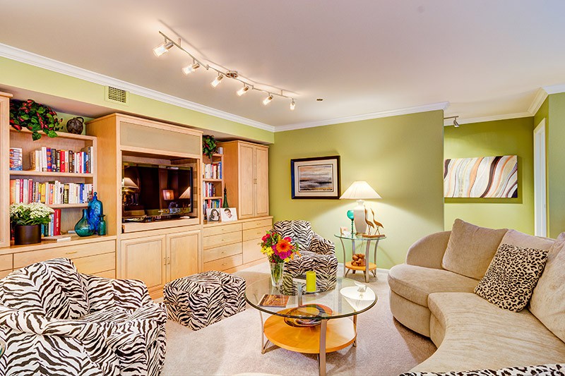 A cozy living room with modern lighting, featuring green walls and zebra-print furniture accents.