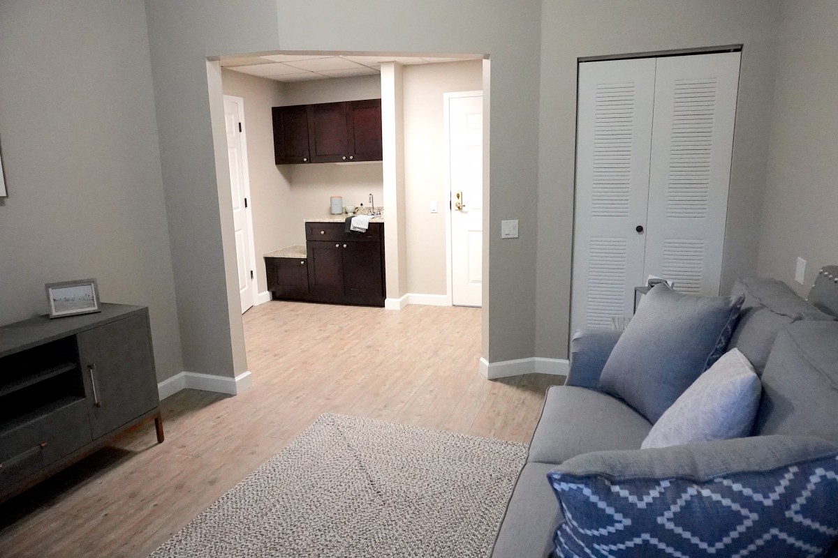 A cozy living room with a sofa and stylish pillows, leading to a small hallway with cabinets.