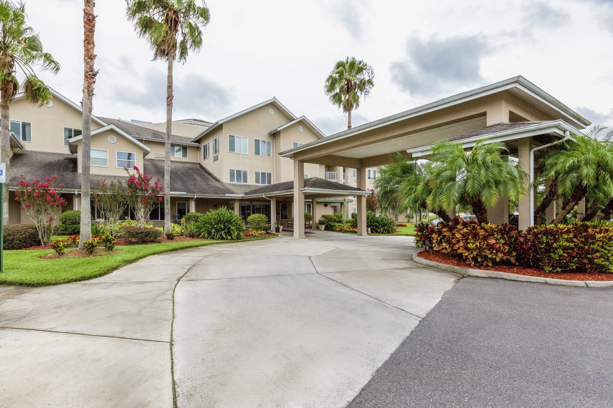 A residential building with a covered driveway, surrounded by palm trees and landscaping under an overcast sky.