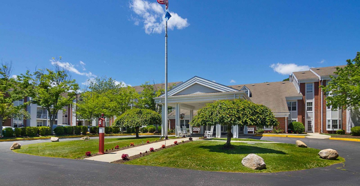 The front entrance of a hotel with well-maintained landscaping and a flagpole on a sunny day.